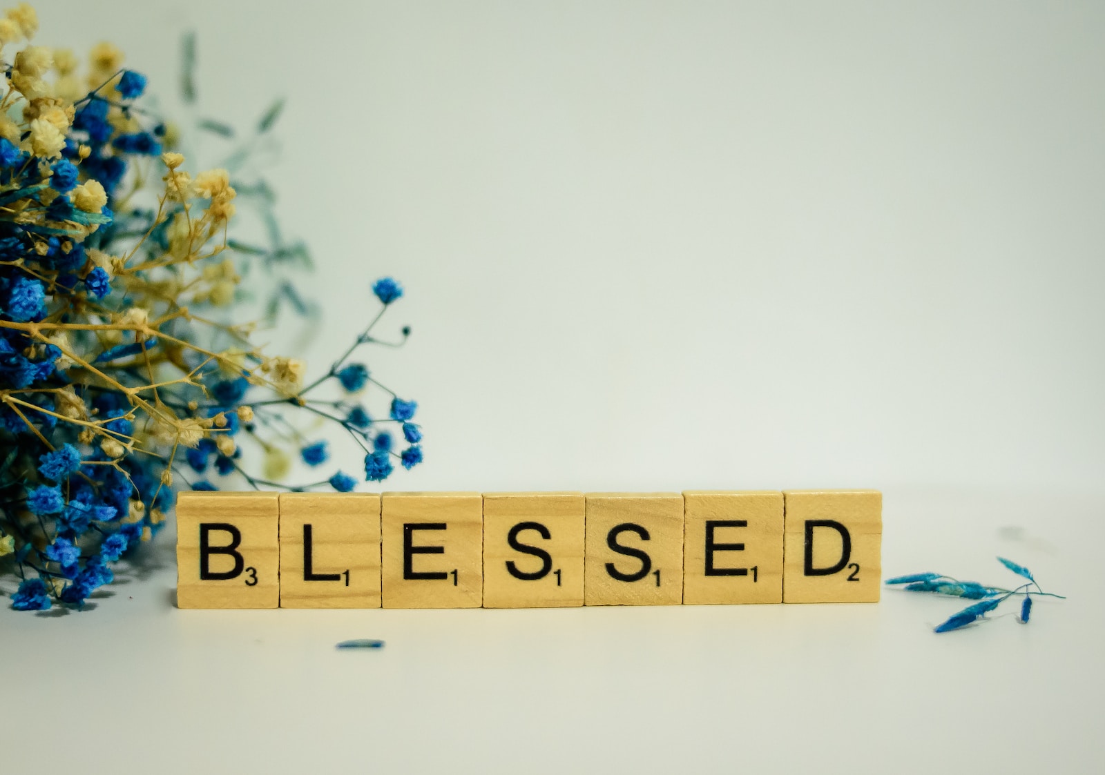 a wooden block spelling the word blessing next to a bouquet of blue flowers